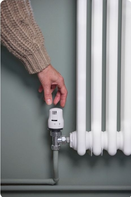 Close-up of a person’s hand adjusting a thermostatic radiator valve — controlling heating efficiency at home.