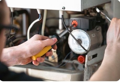 Gas engineer performing maintenance on a boiler system with a screwdriver, focusing on internal components.