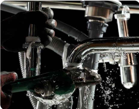 Emergency plumbing repair in progress under a leaking sink, with water spraying from a burst pipe — Tunbridge Wells plumbing response.