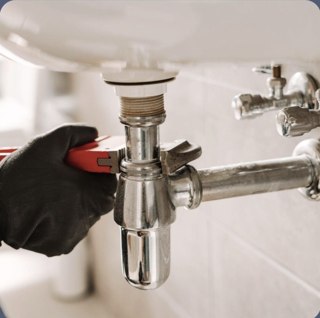 Plumber using a wrench to tighten a chrome pipe connection, representing expert plumbing repairs and pipework services in Rotherfield.