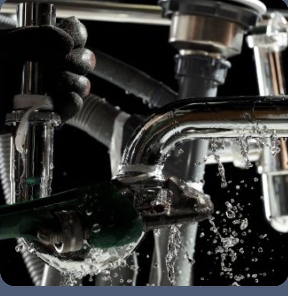Emergency plumbing repair in progress under a leaking sink, with water spraying from a burst pipe — Tunbridge Wells plumbing response.