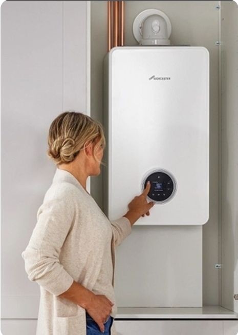 Woman adjusting a modern Worcester Bosch combi boiler touchscreen in a tidy kitchen — smart home heating controls.