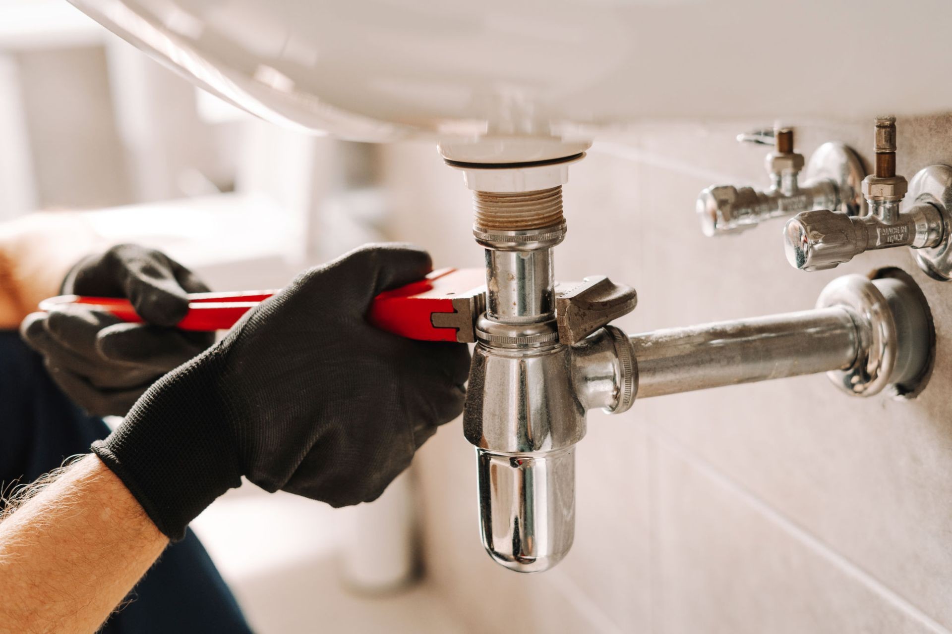 Close-up of a plumber tightening a chrome pipe under a sink using a red wrench — expert plumbing repair service in Crowborough.