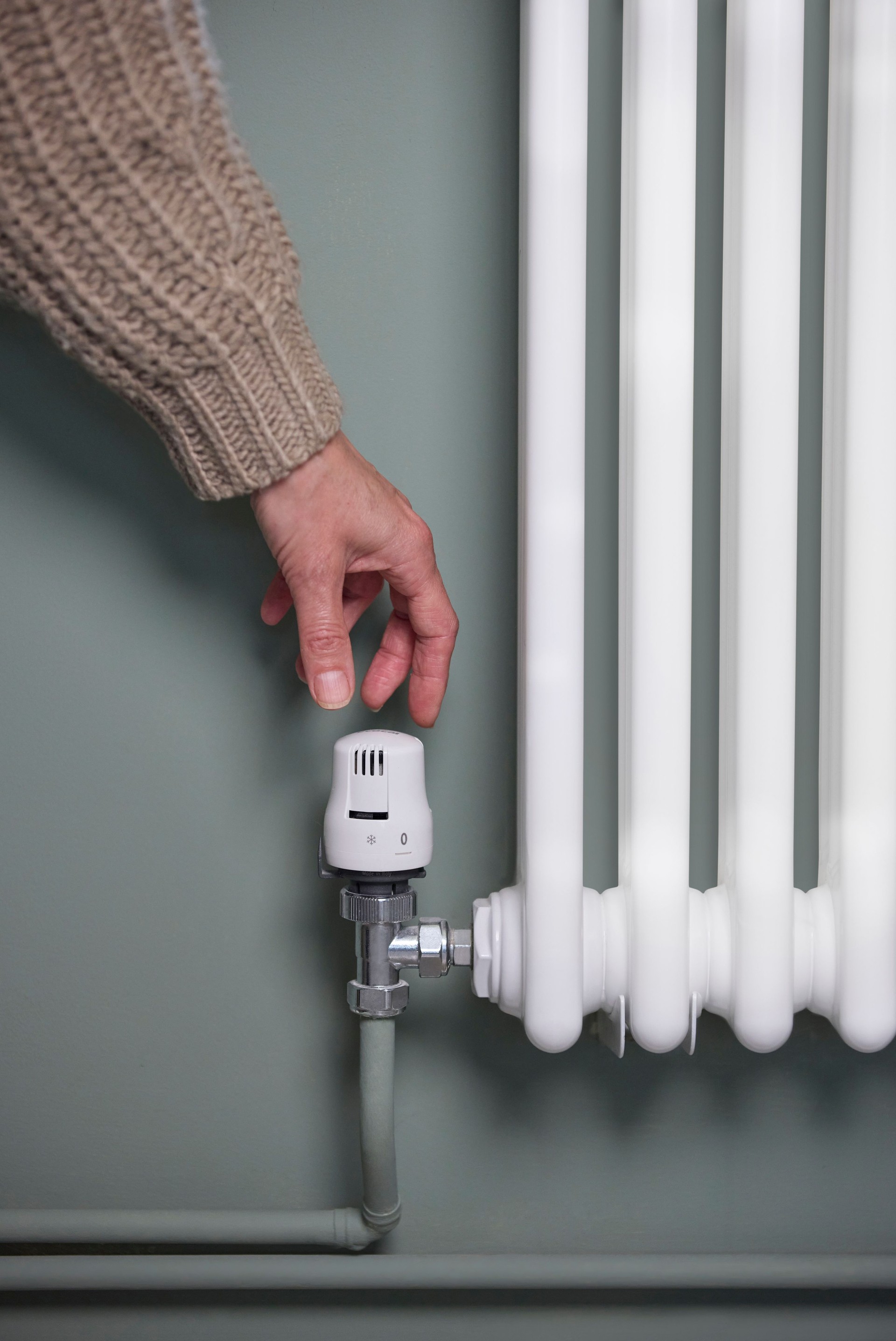 Close Up Of Hand Turning Down Thermostat On Radiator At Home To Save Energy And Money